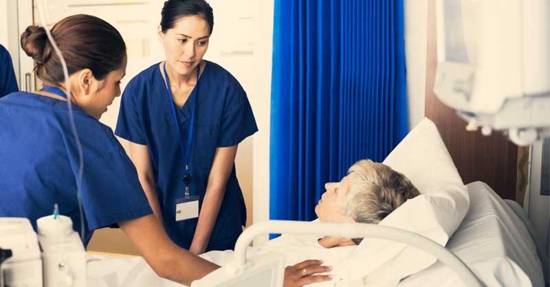 nurses by patient bed helping patient