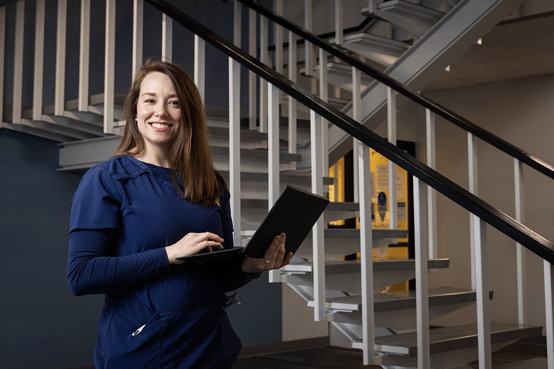 Averett ABSN student standing by stairs holding laptop