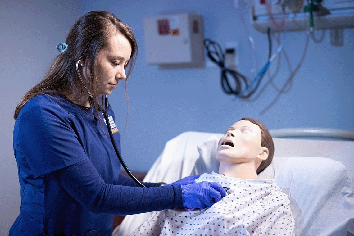 ABSN student using stethoscope on sim manikin