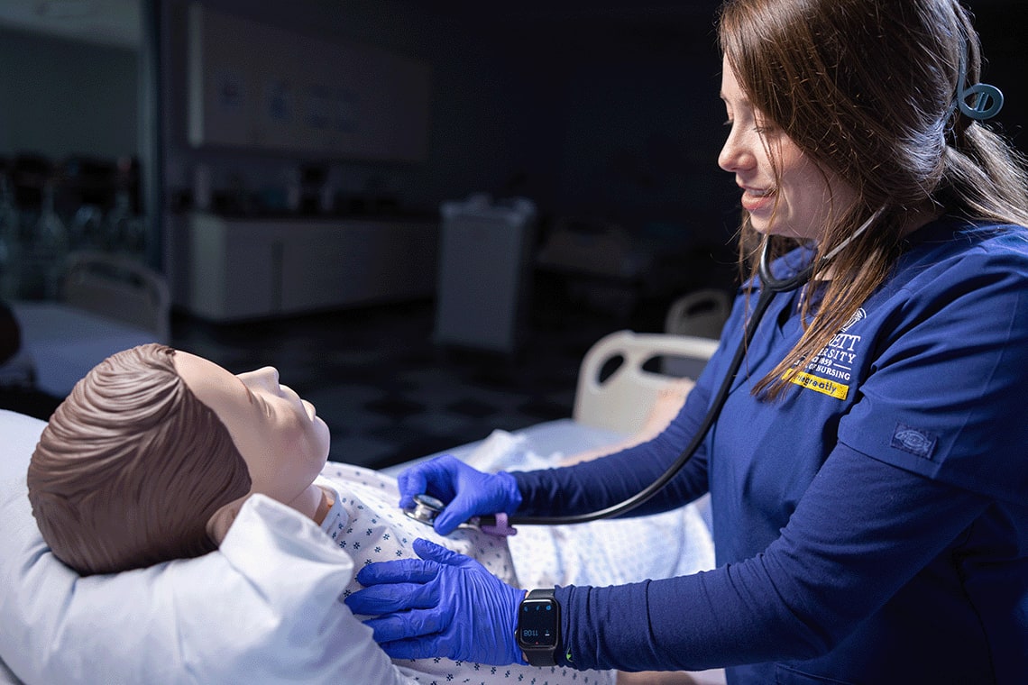 closeup of ABSN student using stethoscope on sim manikin