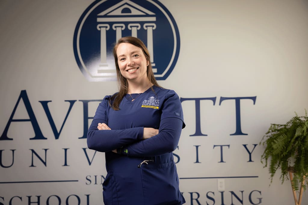 smiling Averett nursing student standing by University wall logo