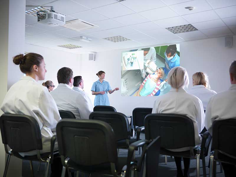 nurse standing in room giving presentation to people in chairs