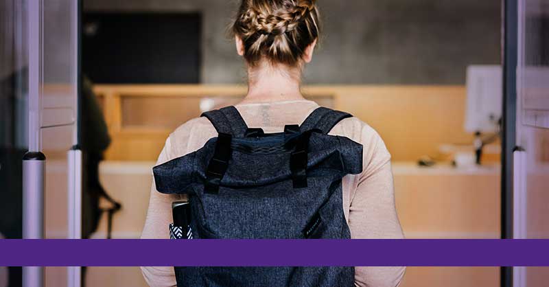 student with backpack walking into building