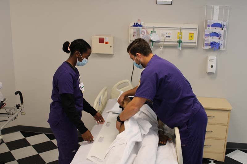 ABSN student helping another student in sim lab