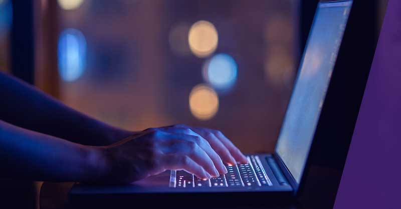 Close-up of hands typing on a laptop in a dark room