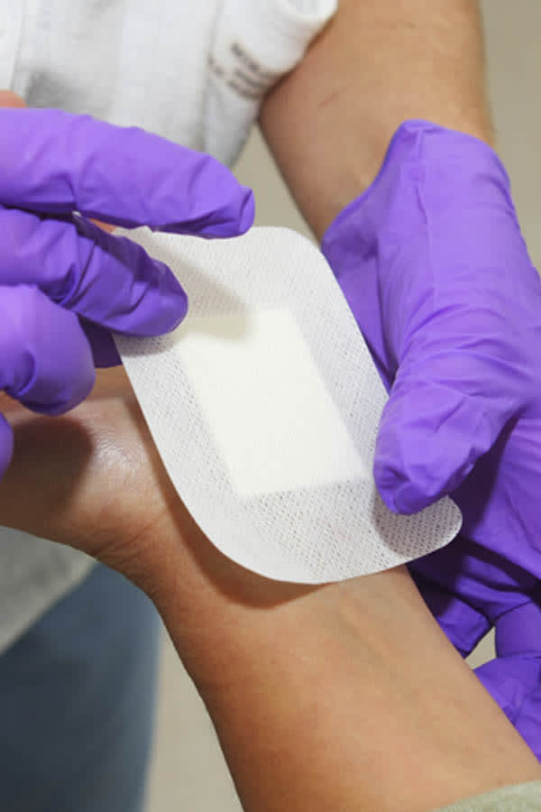 hands with purple gloves adding bandage to another hands wrist