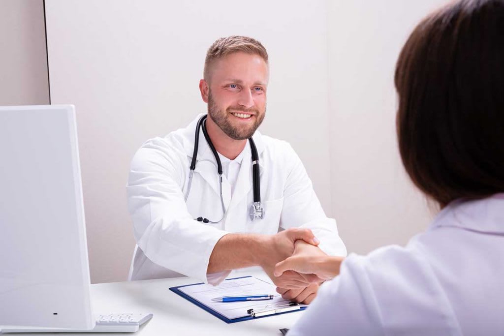 man with white coat sitting and shaking hand of person across from them