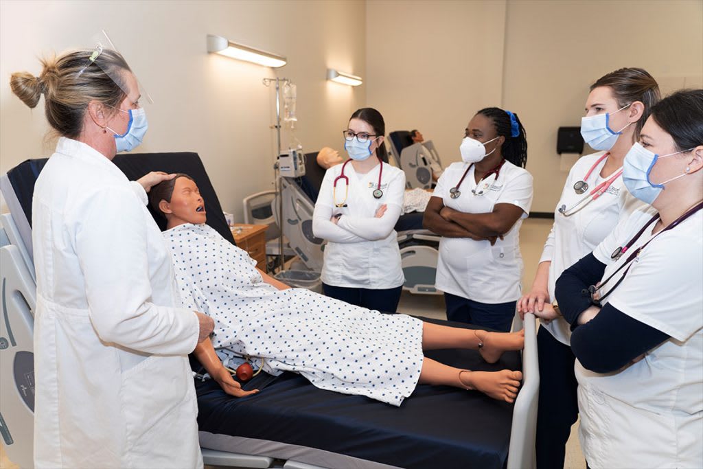 nursing students standing with instructor next to sim manikin