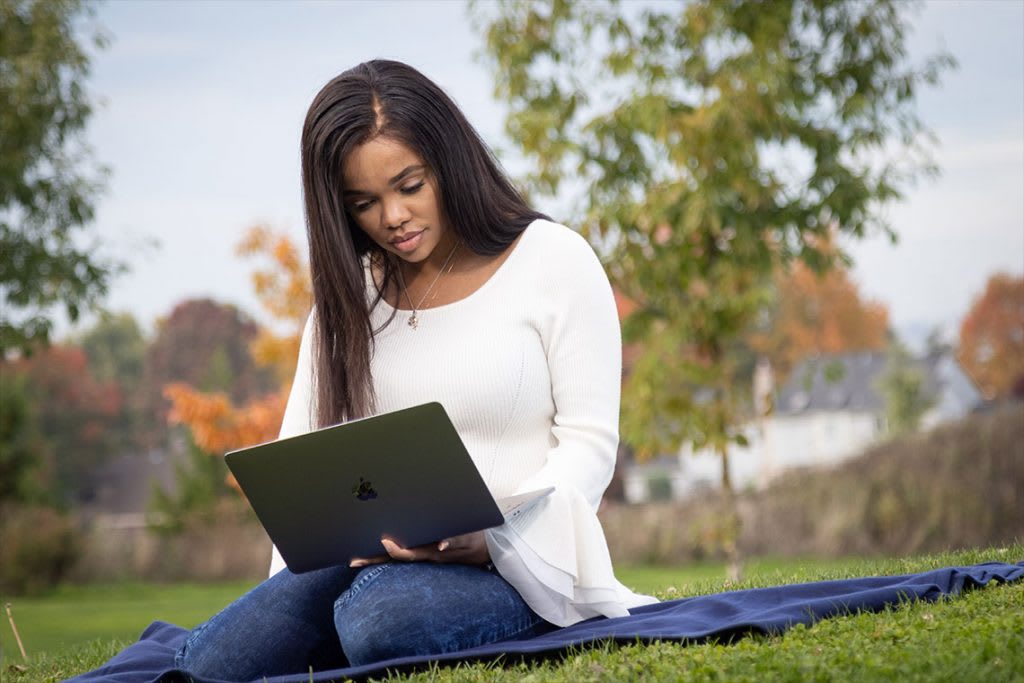 Girl sitting on blanket with laptop in the grass