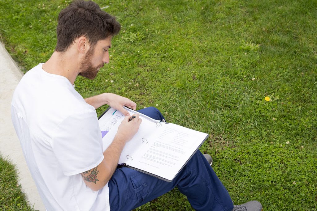 nursing student sitting in grass writing in binder