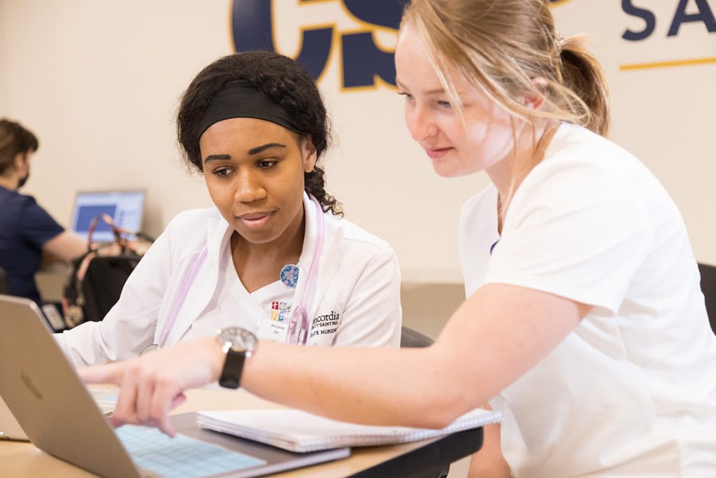 two nursing students sitting and looking at a laptop