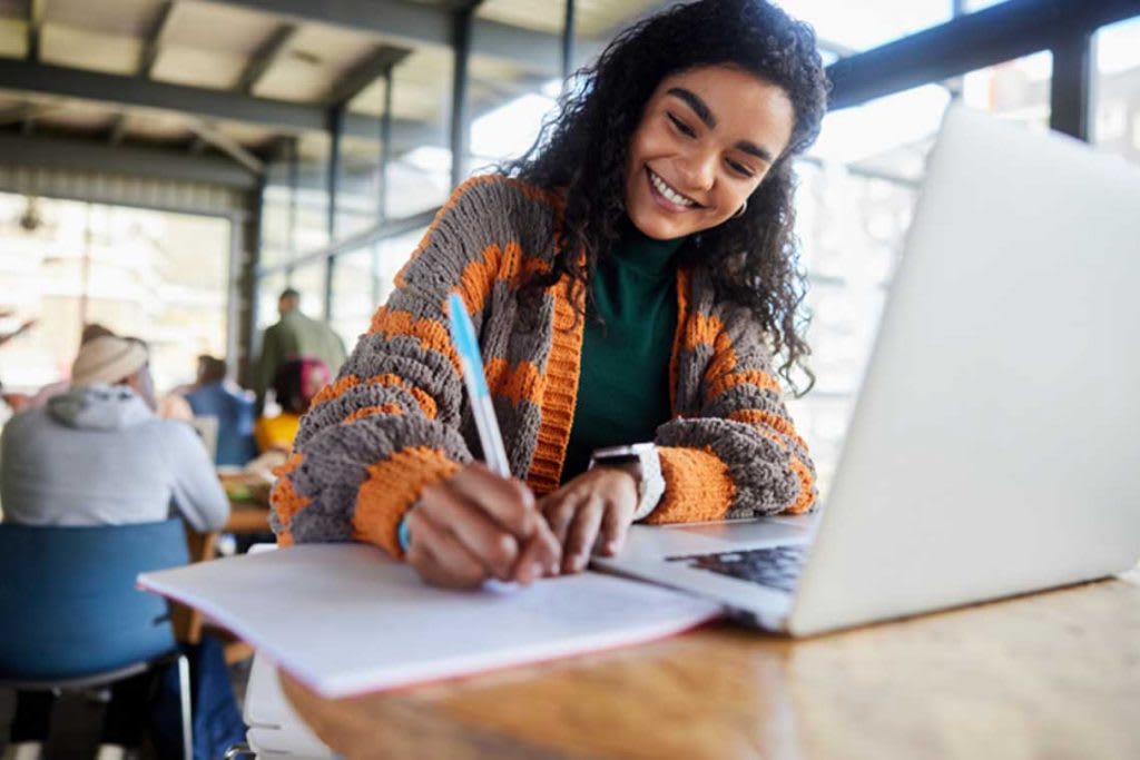 woman sitting down writing and working on laptop