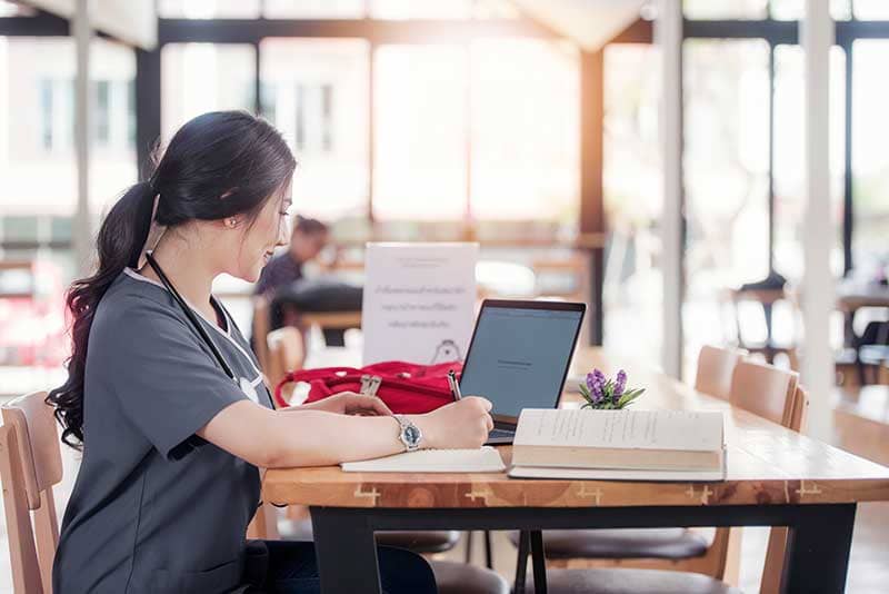 nursing student studying at desk with textbooks and laptop