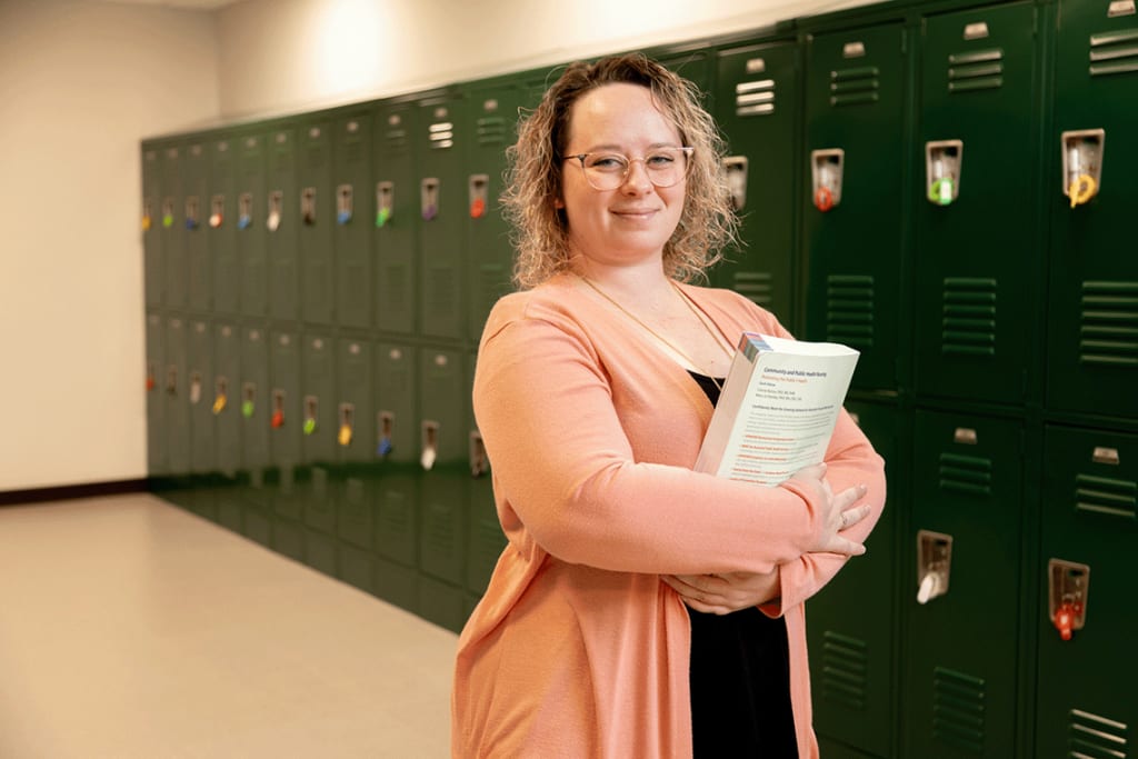 Felician ABSN student standing by lockers holding book