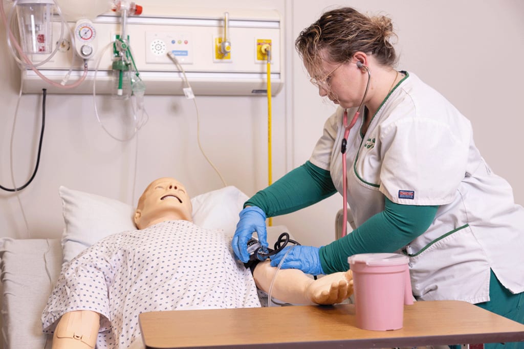 Felician nursing student using blood pressure cuff on sim manikin