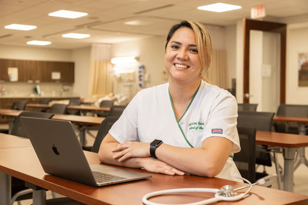 Felician ABSN student sitting at desk with laptop smiling