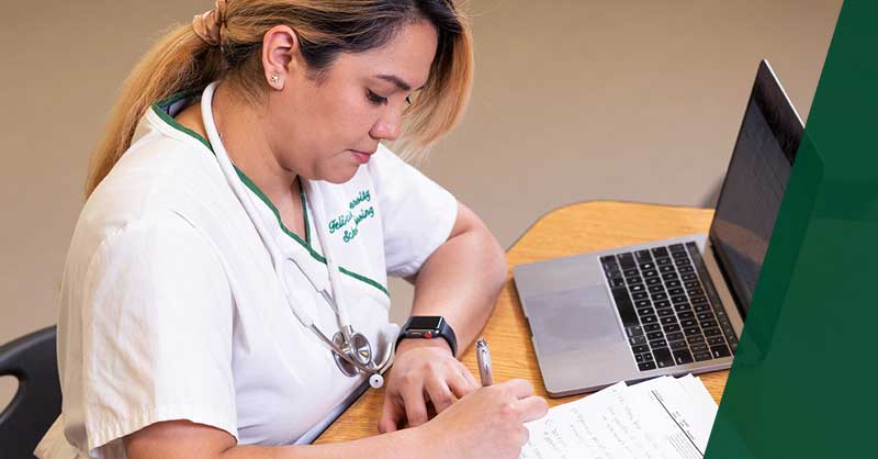 Felician ABSN student writing notes at a desk