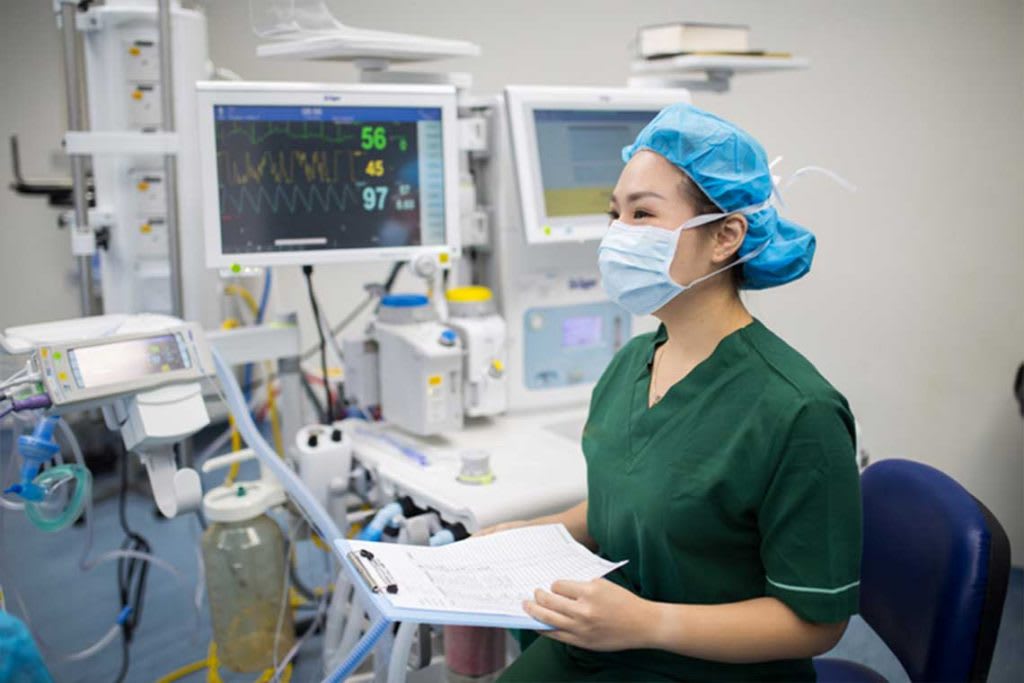 nurse wearing mask and green scrubs standing in front of lab equipment