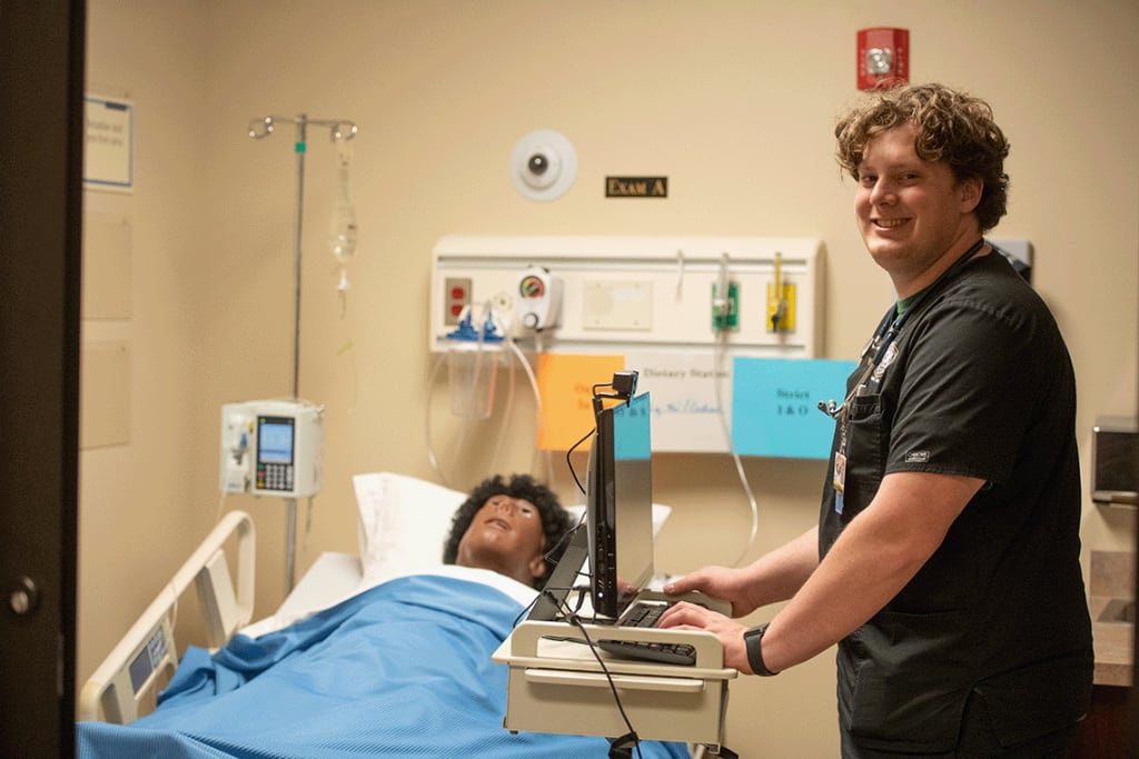 nursing student smiling while on computer next to manikin