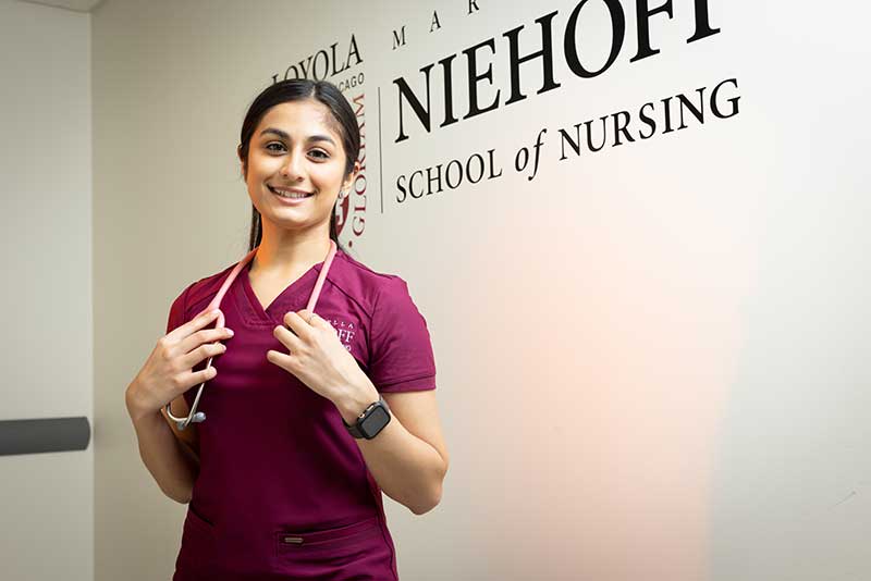 nursing student standing in front of Loyola Nursing wall sign