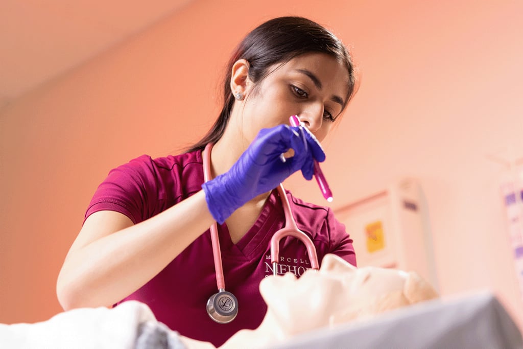 Loyola nursing student standing above manikin shining light