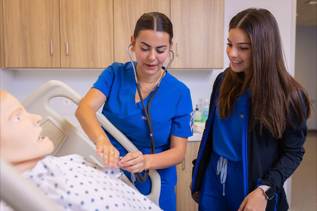 two Madonna ABSN students working with sim manikin