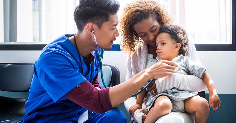 Male nurse in blue scrubs checking child's heartbeat