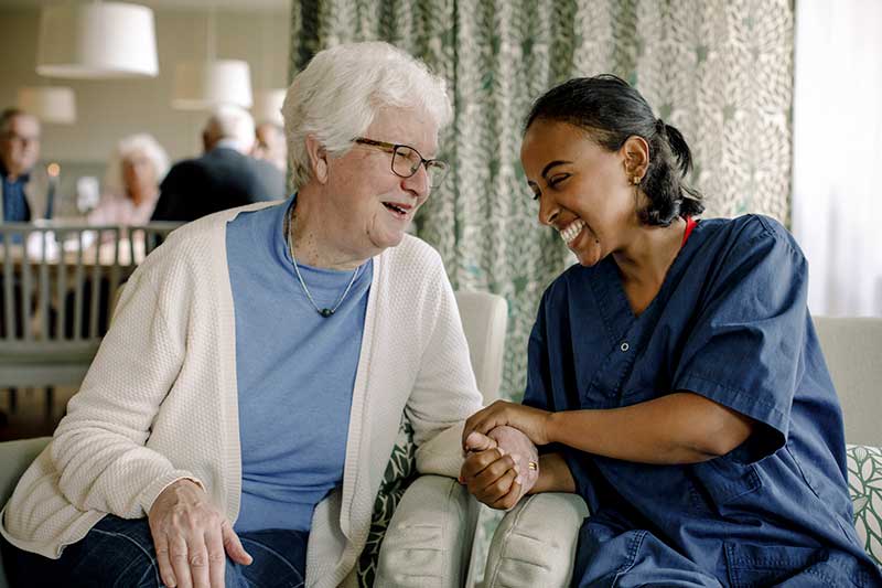 nurse sitting with elderly patient holding their hand