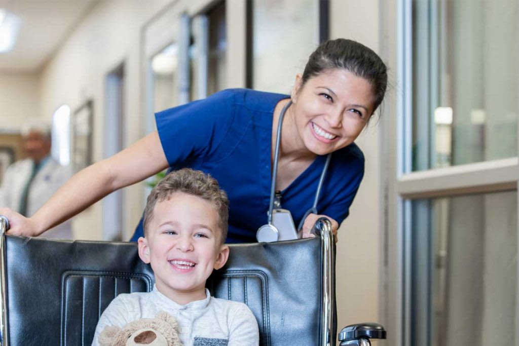 Nurse in blue scrubs pushing child in wheelchair