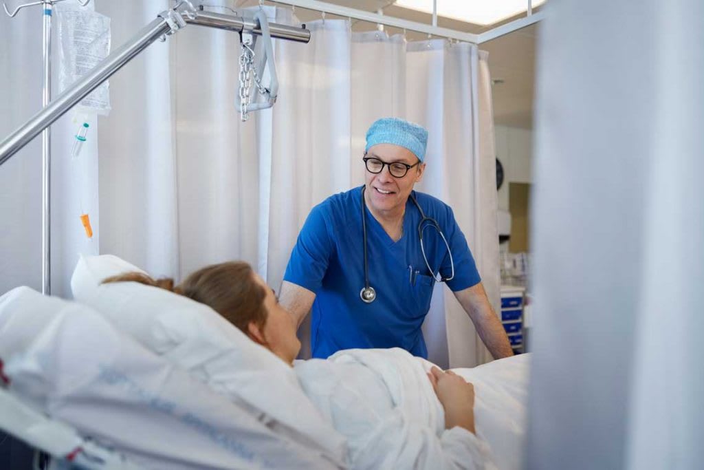 older nurse talking to patient in hospital bed