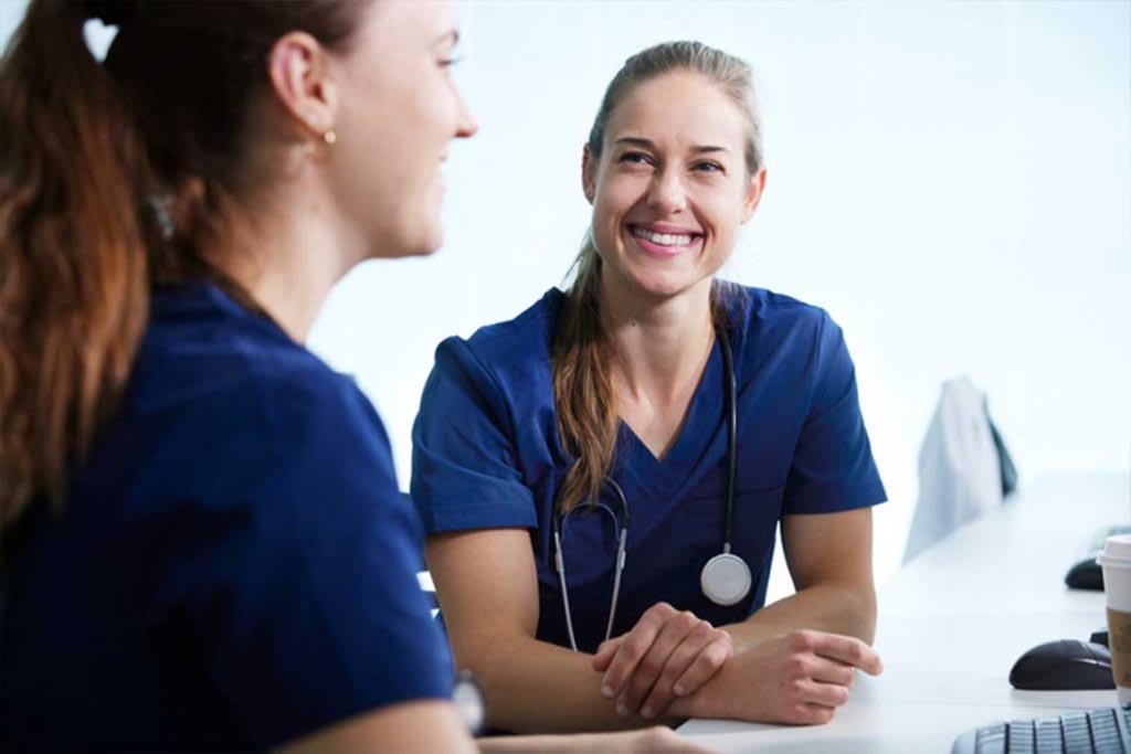 two nurses in blue scrubs sitting and talking