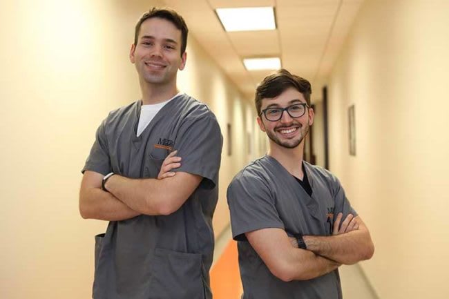 two nursing students in gray scrubs standing and smiling