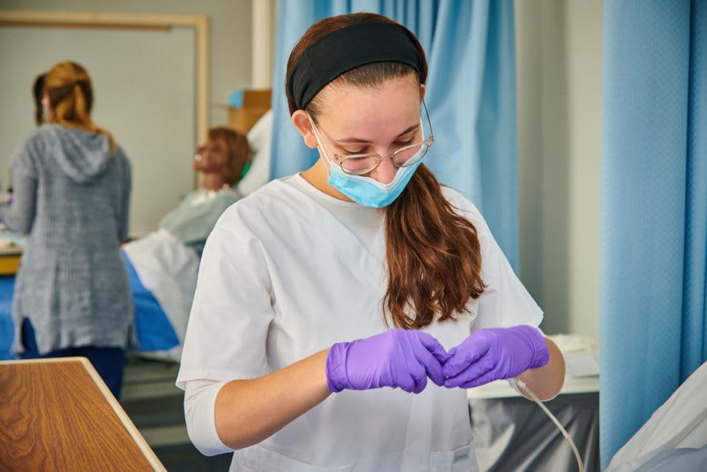 Nursing student in lab setting with purple gloves