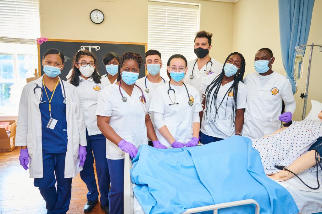 9 nursing students smiling over a practice manikin