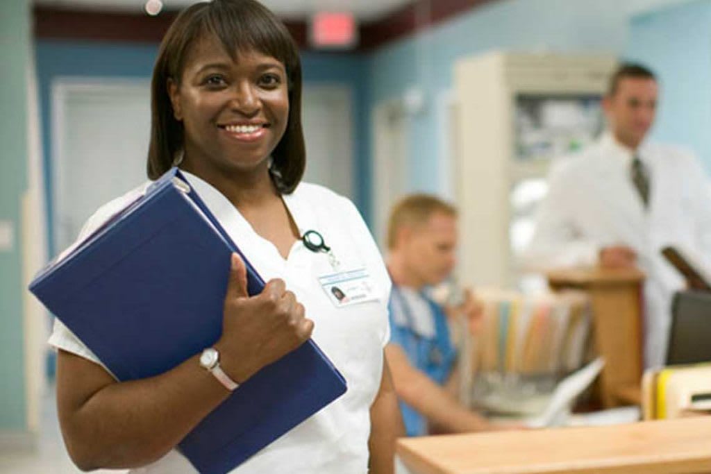 nurse in hospital with folder in arms smiling at camera