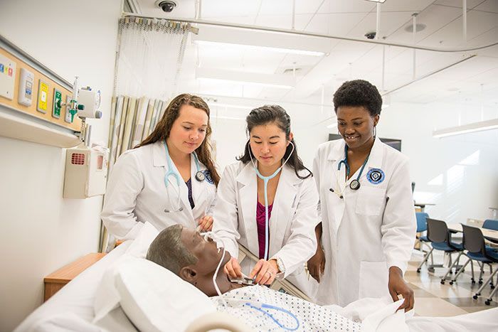 three NDMU nursing students with lab coats working with a simulation manikin