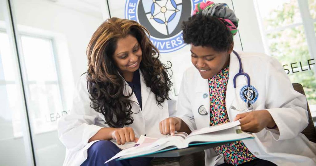 two nursing students looking at textbook together