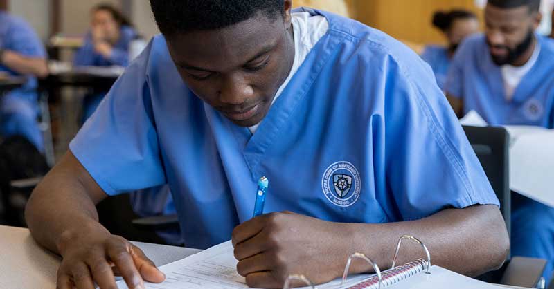 ABSN student writing down notes at desk