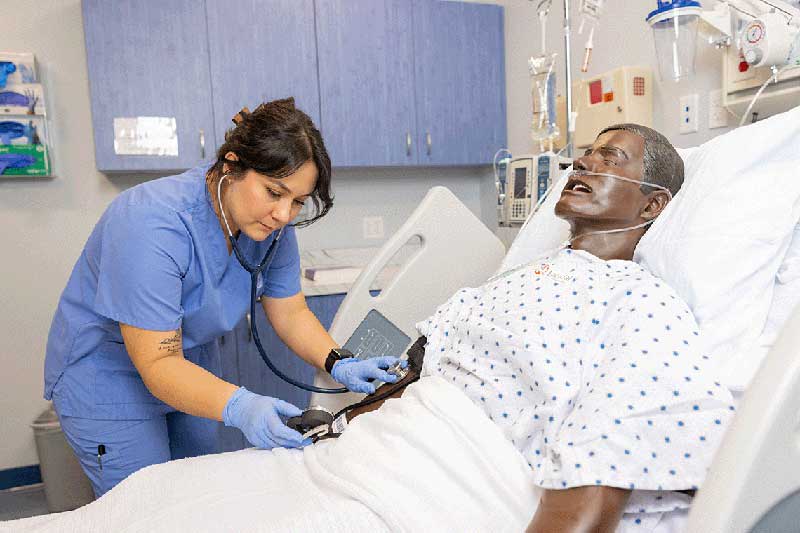 NDMU student in blue scrubs working on manikin