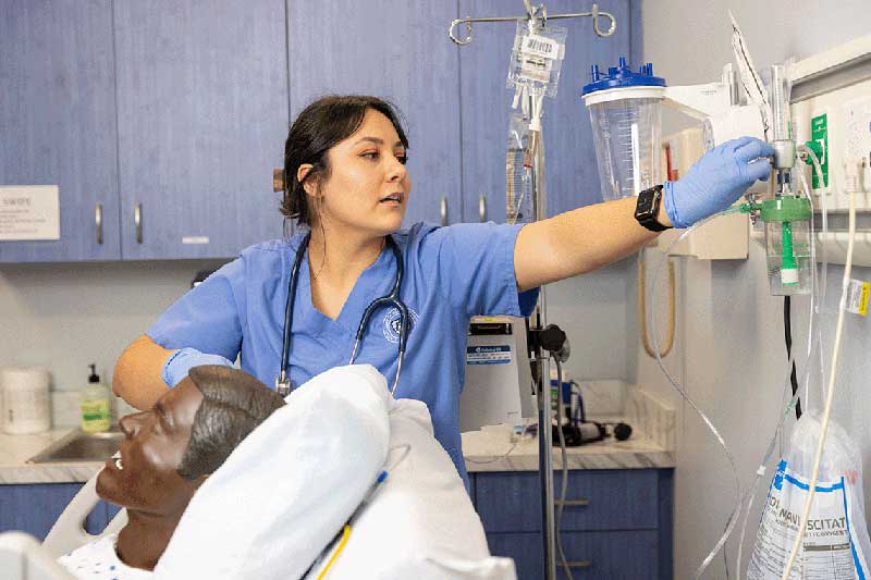 NDMU student in blue scrubs working on manikin