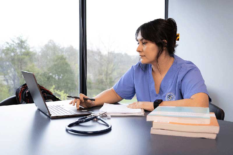 NDMU student in blue scrubs working on computer