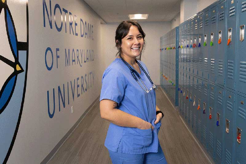 NDMU student in scrubs smiling in front of lockers