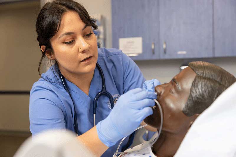 NDMU student in blue scrubs working on manikin