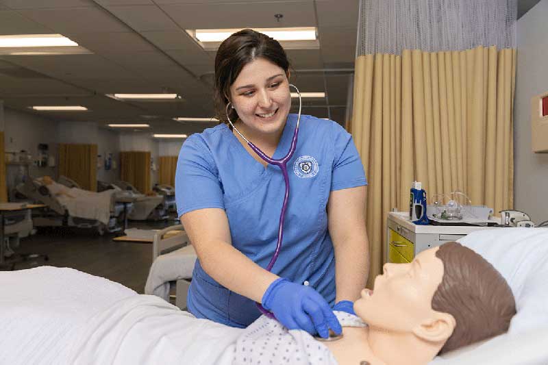 NDMU student in blue scrubs working on manikin