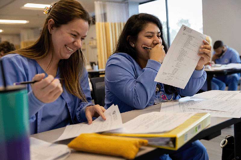 2 NDMU students smiling while doing coursework