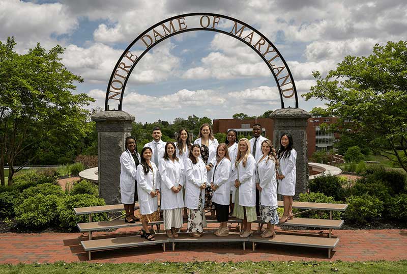 13 NDMU students standing in front of campus sign