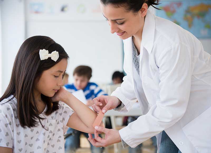 school nurse helping child with band-aid in classroom