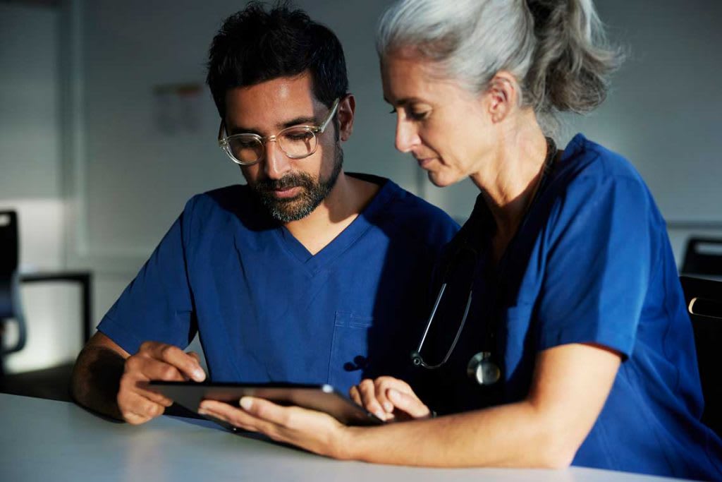 two nurses sitting at desk looking at tablet