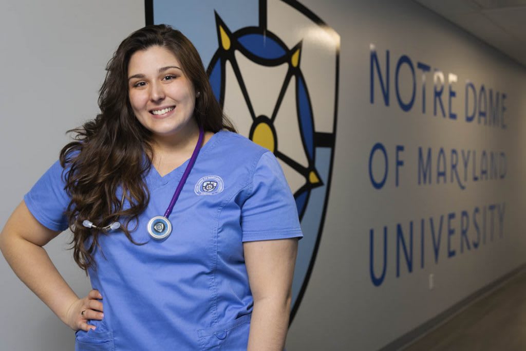 student nurse in front of NDMU logo on wall