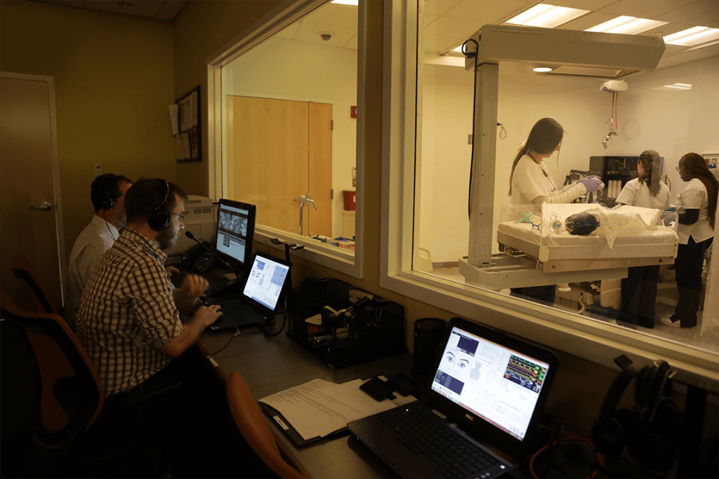 people monitoring nursing skills lab behind window